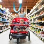 A woman shops in a grocery store while pushing a stroller with a child